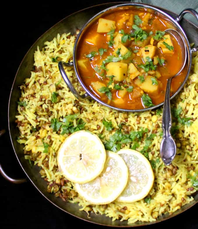 A copper serving tray filled with an Instant Pot Khichdi with Mung Bean Sprouts and a bowl with a red potato curry sits inside the server. Slices of lemon are to the side.