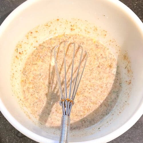 Flaxmeal mixture with whisk in white bowl.