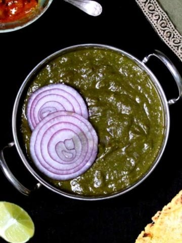 A top close up shot of sarson ka saag with makki di roti on the side and indian pickles