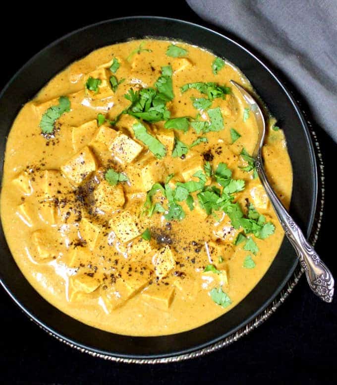 Round black bowl with a creamy sauce and cubes of white tofu and green cilantro