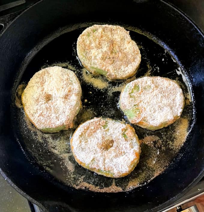 Green tomato slices frying in cast iron skillet.
