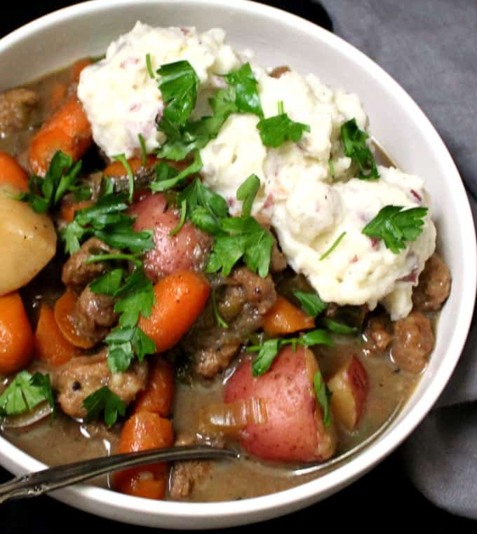 A close shot of a hearty bowl of vegan Irish "lamb" stew with creamy mashed potatoes, carrots, celery and parsley