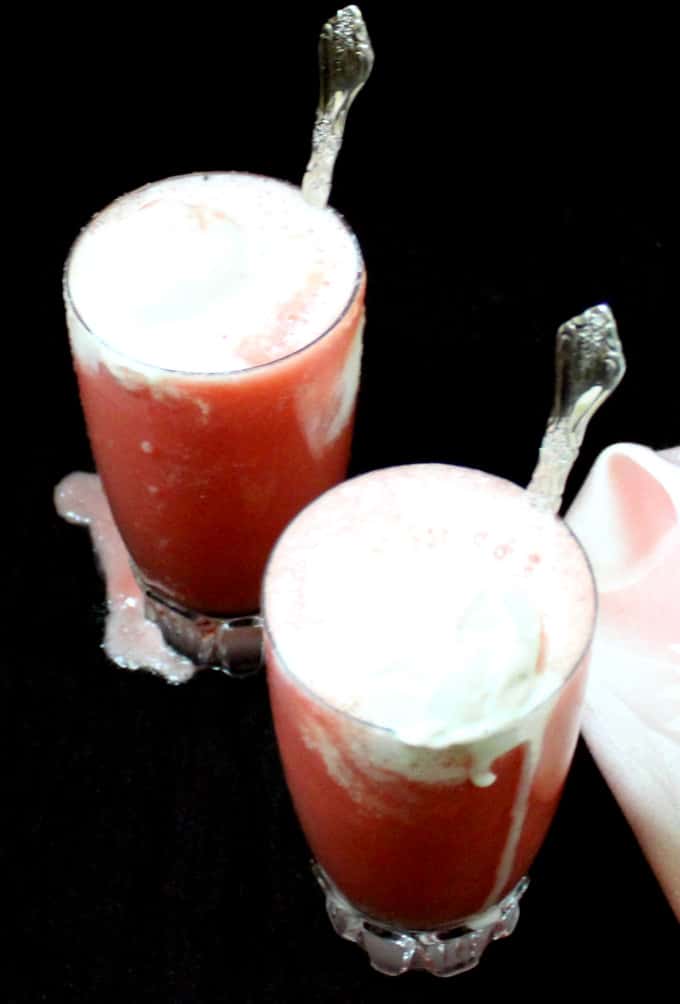 Watermelon smoothies in two tall glasses with ice cream and spoons.