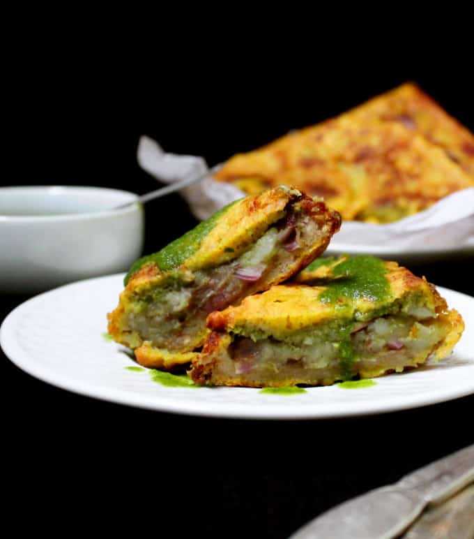 Two pieces of bread pakora with potato stuffing, tamarind chutney, green chutney and chaat masala.