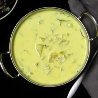 Creamy Green Tomato Stew in a karahi bowl with a spoon on the side and stir-fried mushrooms