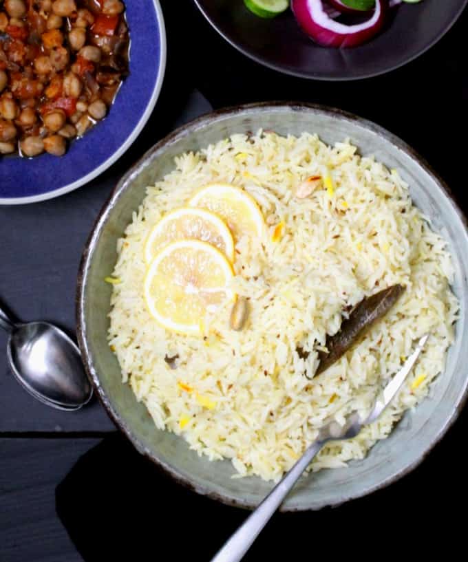 Top shot of a big bowl of jeera rice or cumin rice with chana masala in a blue bowl on the side