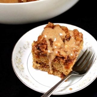A slice of vegan cinnamon cake with a swirled cinnamon filling and cinnamon streusel topping and gooey vanilla cinnamon glaze sitting on a white plate with a fork