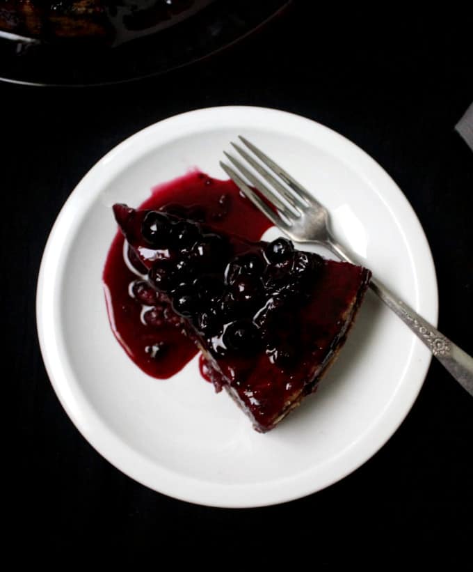 Top shot of a big slice of vegan lemon blueberry cake with blueberry topping on a white plate with a fork