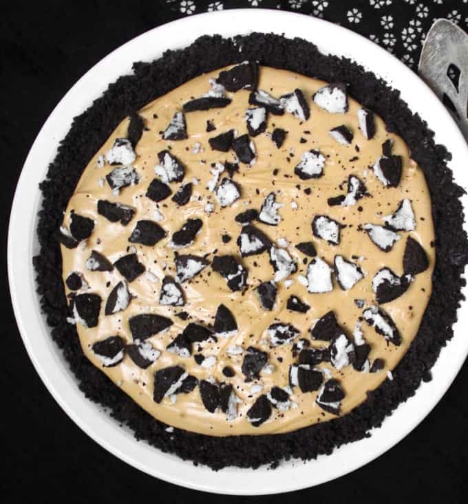 Overhead shot of a vegan peanut butter oreo pie  in white ceramic pie plate with pie server and black and white napkin.