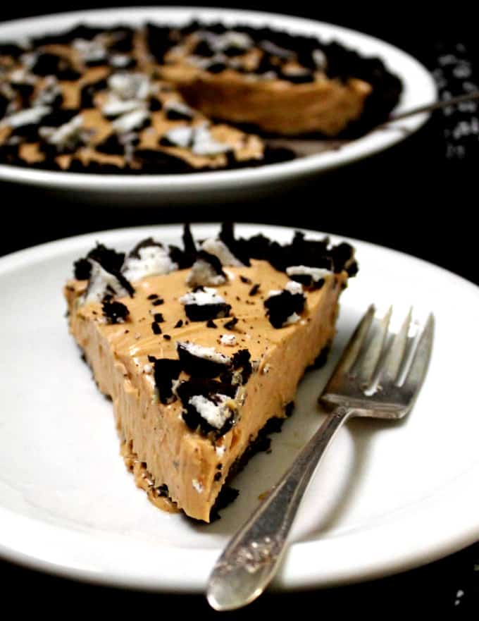 A slice of a delicious vegan peanut butter oreo pie with cookies crumbled on top, in a white plate with a fork