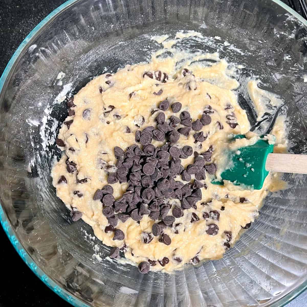 Chocolate chips added to cookie dough in glass bowl.