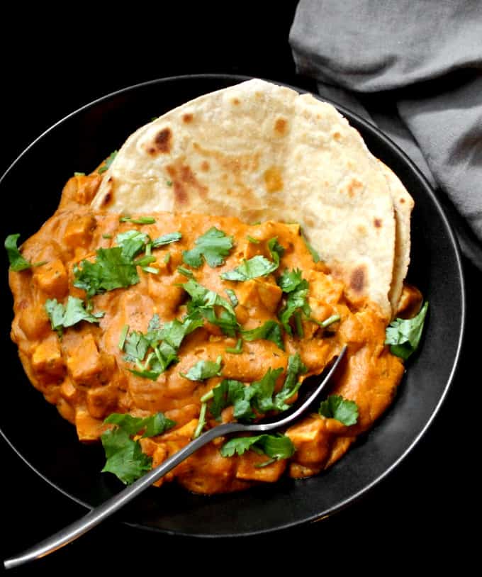 Vegan paneer butter masala in a bowl with roti and cilantro garnish.