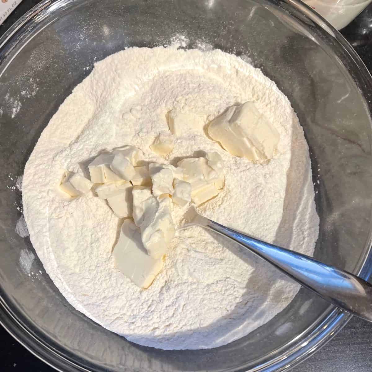 Butter added to dry ingredients for biscuits in bowl.