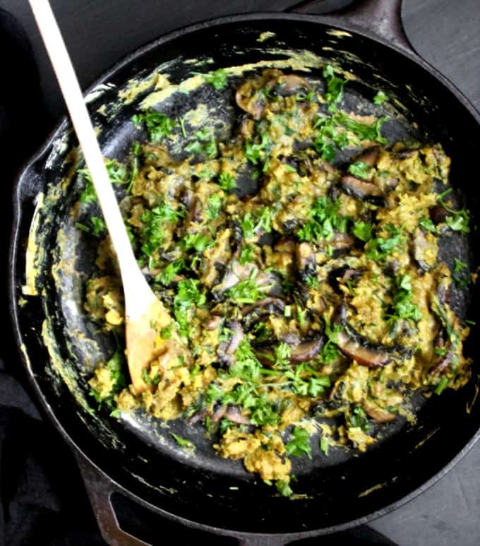 Black cast iron skillet with scrambled eggs with mushrooms and spinach and parsley