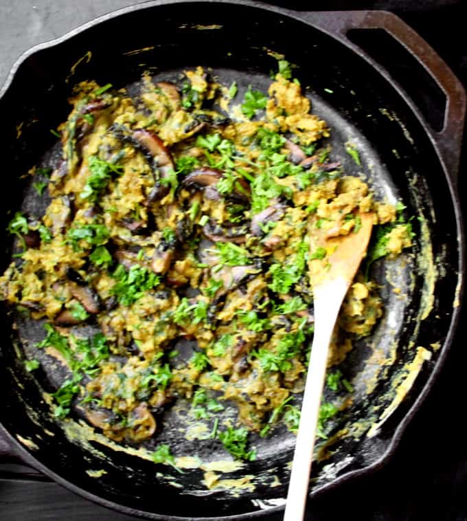 Vegan Scrambled Eggs with Mushrooms and Spinach in a black cast iron skillet with a wooden ladle