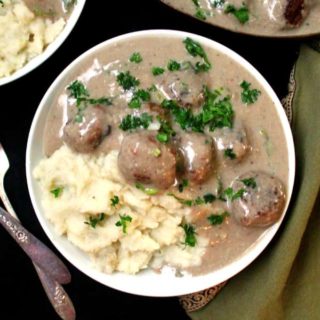 A top closeup of a white bowl of creamy mushroom gravy with vegan meatballs and parsley sprinkled on top