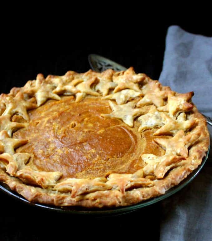 Front partial shot of a baked vegan sweet potato pie with a decorative crust and a gray napkin on the side