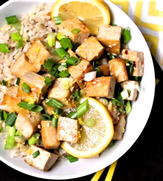 Cubes of glazed lemon tofu on a bed of brown rice with scallions and sesame seeds.