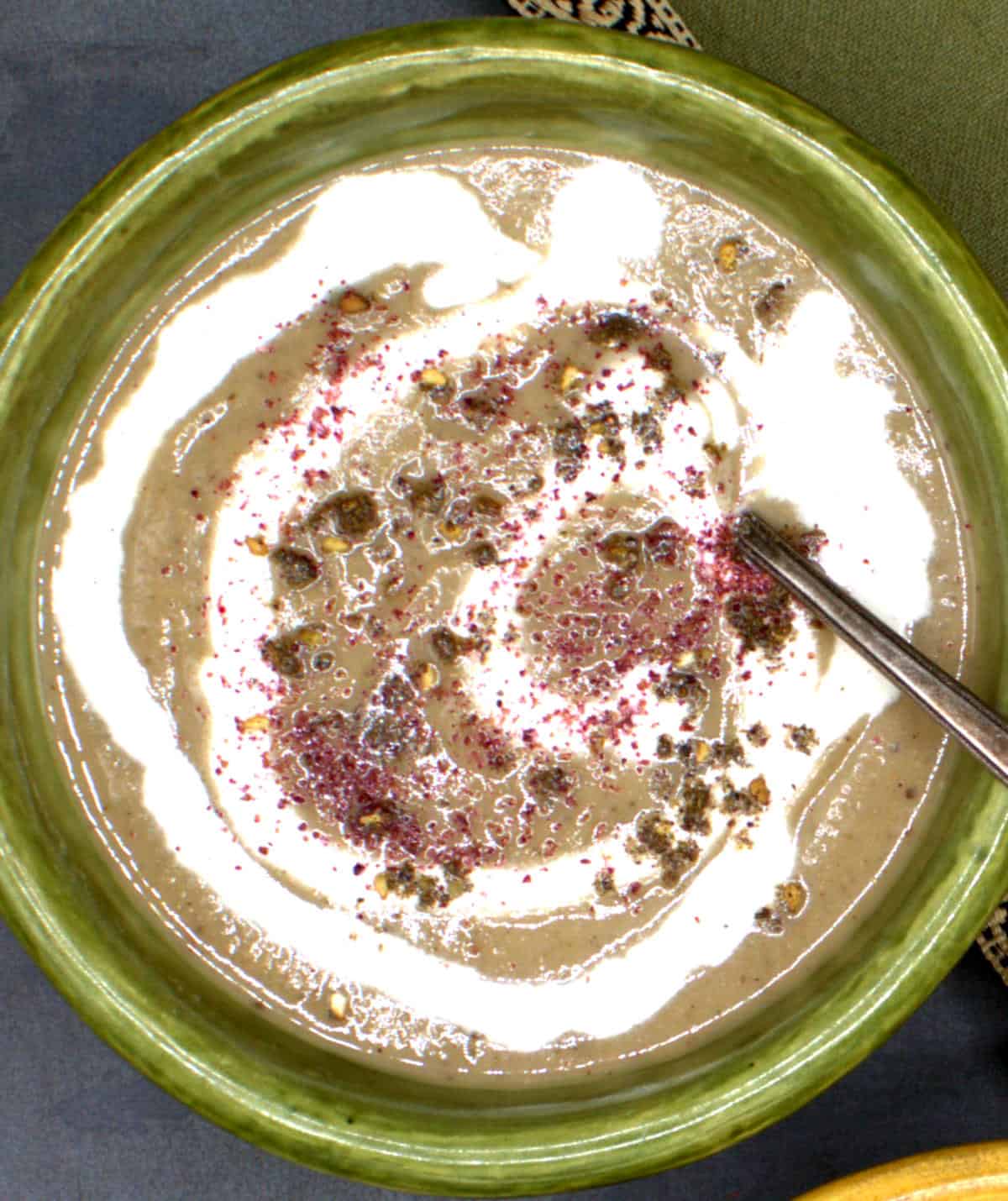 Vegan eggplant soup with cashew cream and za'atar in green bowl with spoon.