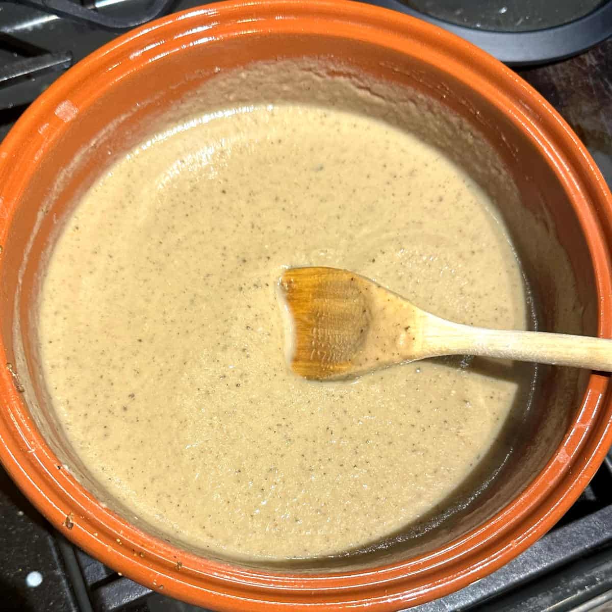 Eggplant soup cooking in pot with wooden ladle.