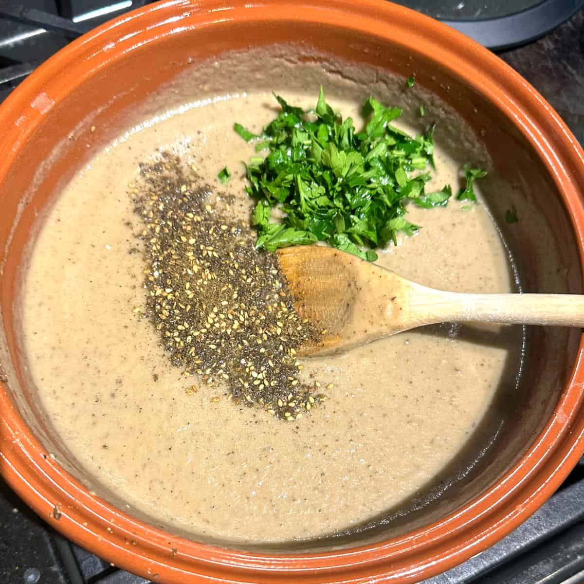 Za'atar and parsley added to eggplant soup in pot.