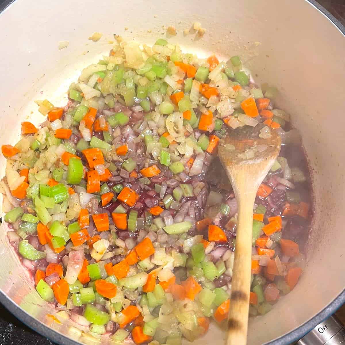 Garlic and vegetables added to Dutch oven with spoon.