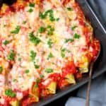 Close up of vegan manicotti pasta in gray baking dish with silver spoon