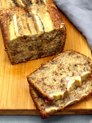 Sliced vegan banana bread on chopping board with gray napkin.