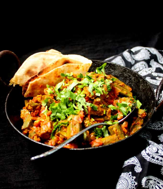 Bhindi masala in a black kadhai with a silver spoon and a black and white paisley napkin