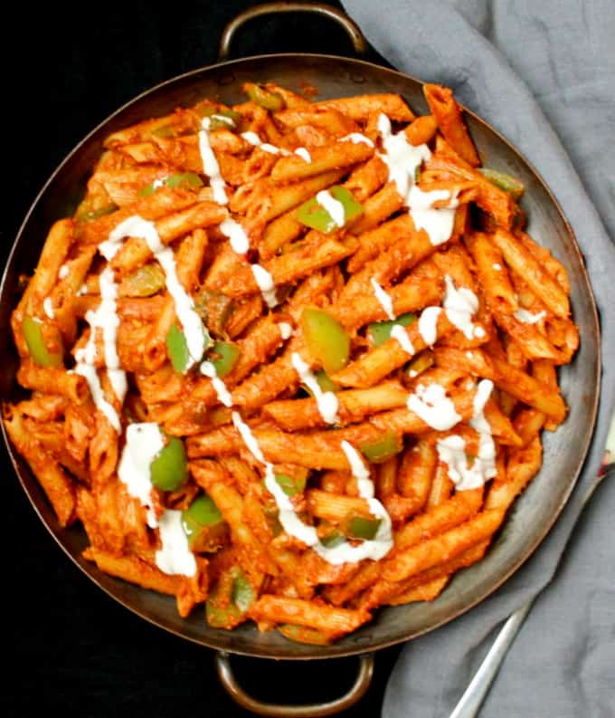 An overhead shot of masala pasta cooked in the Indian street food style in a copper container with a serving spoon.