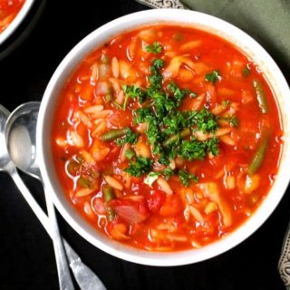 Top shot of a bowl of perfect minestrone soup with parsley garnish, and orzo, beans, carrots, celery, onions, garlic, cabbage and green beans