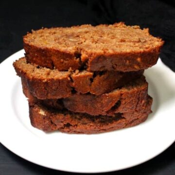 Slices of vegan banana nut bread stacked on a white plate against a dark background.