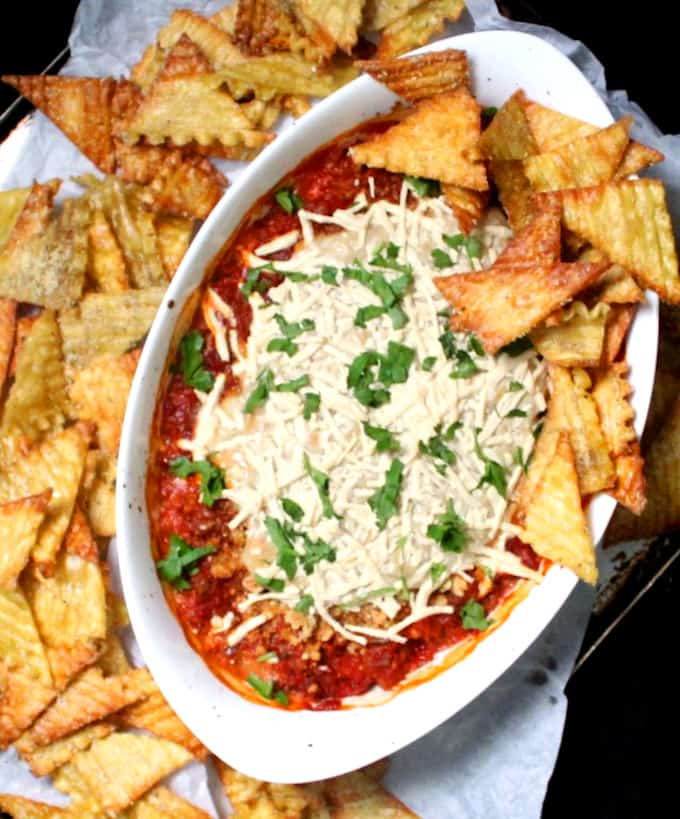 Golden lasagna chips surrounding a lasagna dip in a white baking dish with a tomato sauce topped by vegan mozzarella, parmesan and ricotta