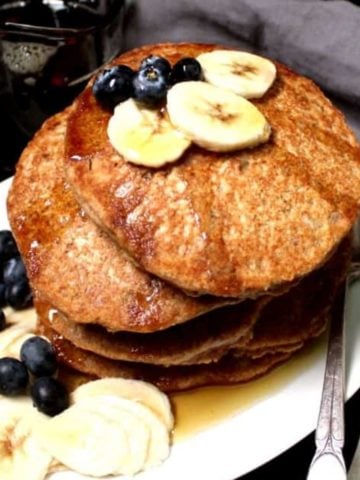 Photo of a stack of whole wheat vegan pancakes with blueberries and slices of banana and maple syrup