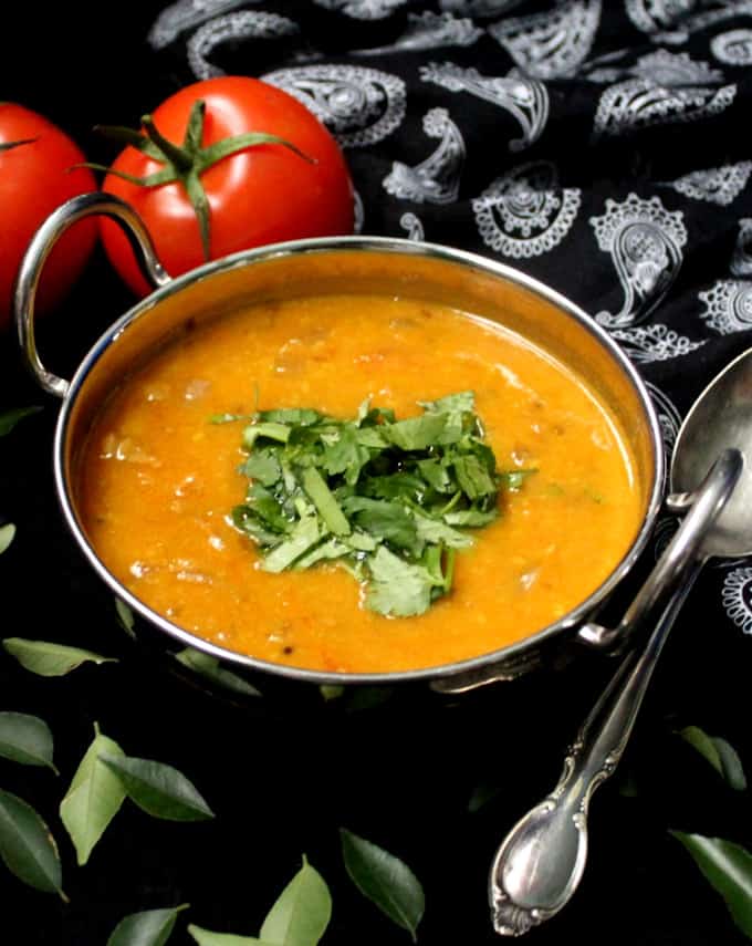 Indian tomato dal in a kadhai with cilantro garnish and tomatoes on the side and a black and white paisley print napkin