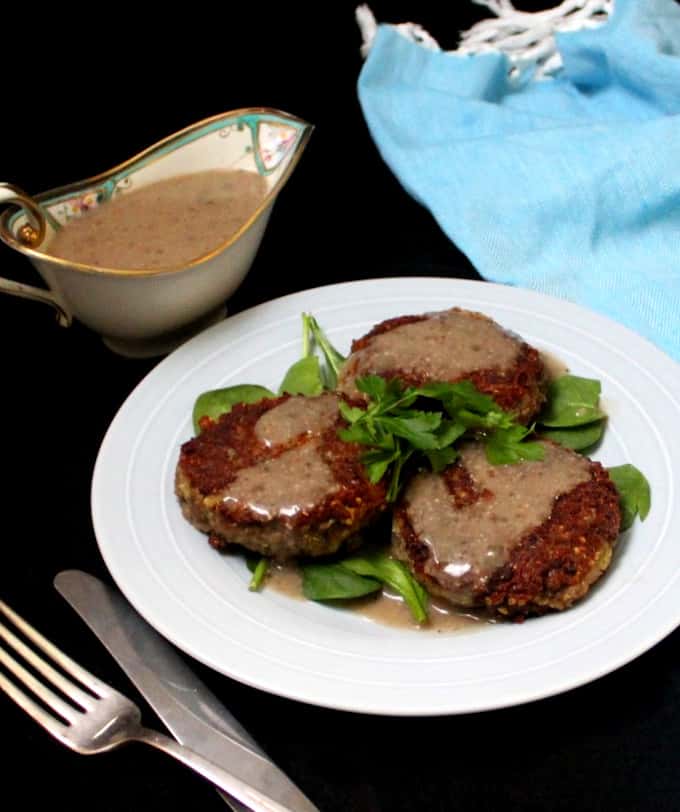 A light blue plate with three vegan quinoa steaks and a sauce boat with mushroom gravy, knife and fork and a blue napkin makes a delicious vegan lunch or dinner