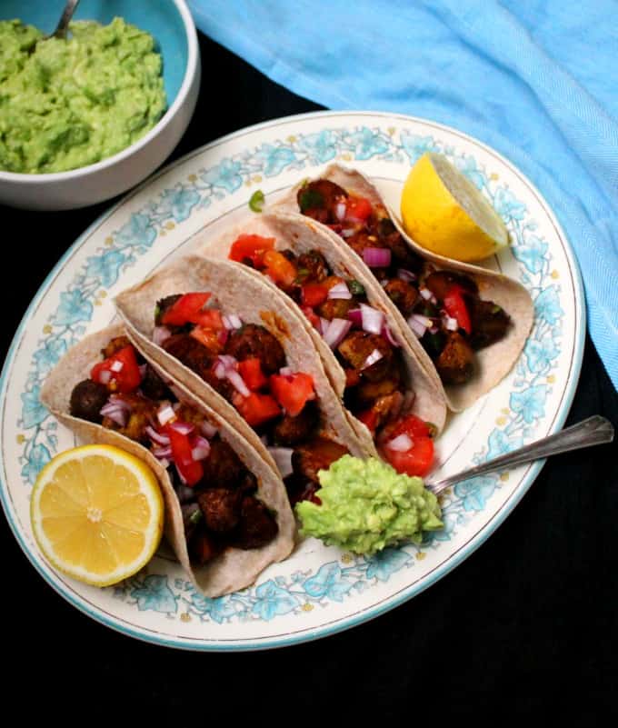 Vegan Potato Tacos with guac and salsa on a plate with guacamole and lemons.