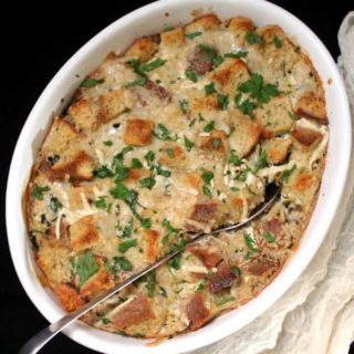 An overhead shot of a white, oval casserole dish with spinach, sausage and cheese casserole and a serving spoon on black background