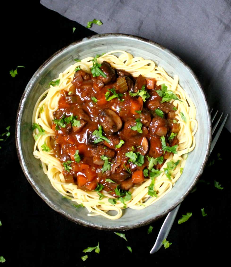 Vegan mushroom bourguignon on a bed of noodles in bowl with parsley garnish.