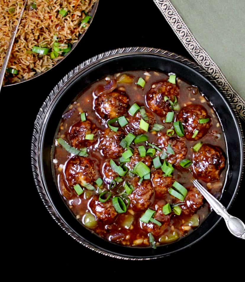Veg Manchurian in a black bowl with chinese fried rice and a green napkin