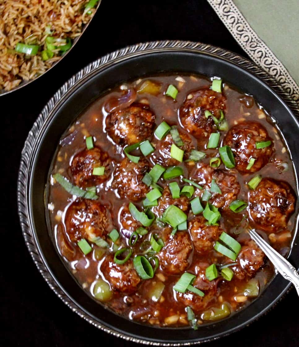 Photo of Veg Manchurian in a black bowl with chinese fried rice and a green napkin
