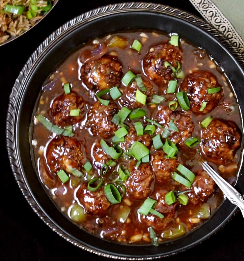 Veg Manchurian in a black bowl with chinese fried rice and a green napkin