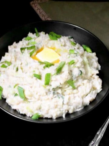 A bowl of vegan colcannon with a pat of vegan butter, scallions and a spoon and green napkin