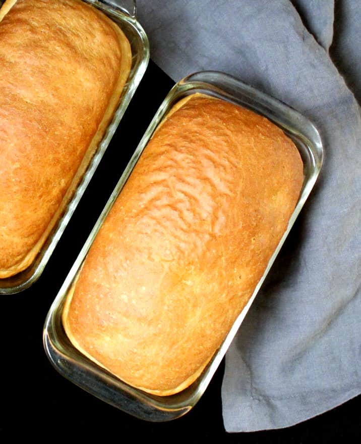 Two loaves of vegan sandwich bread in glass loaf pans with a gray napkin