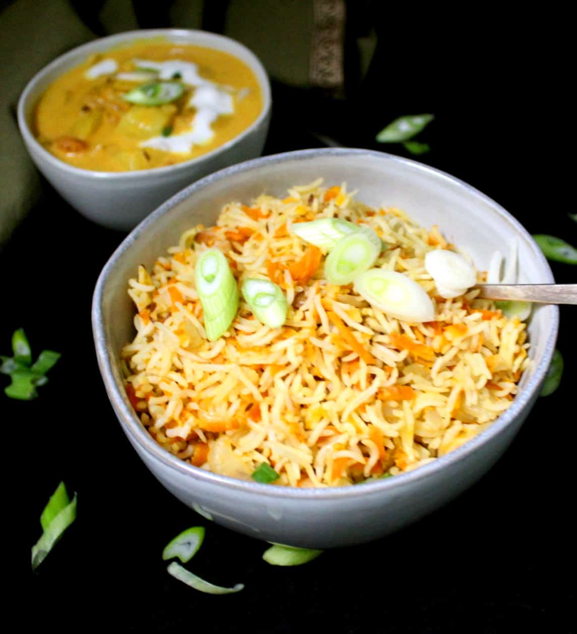 A bowl of carrot rice to be served with a coconut curry pictured in the background.