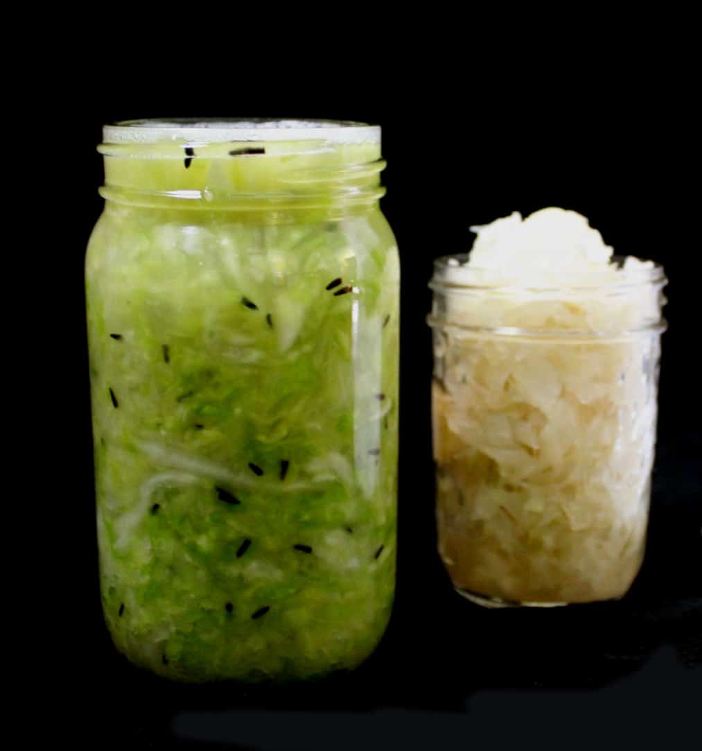 Two jars, one with freshly made sauerkraut and another with a ready sauerkraut standing next to each other on a black background