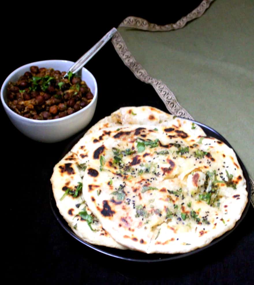 A frontal shot of three aloo kulcha in a black plate with pindi chole