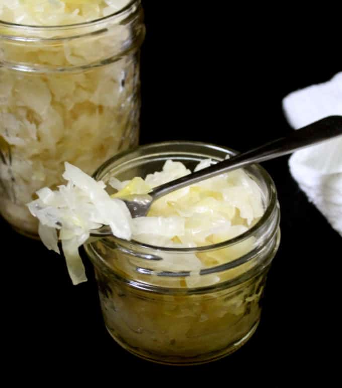 A close up of a mason jar with sauerkraut next to another with a fork on top.
