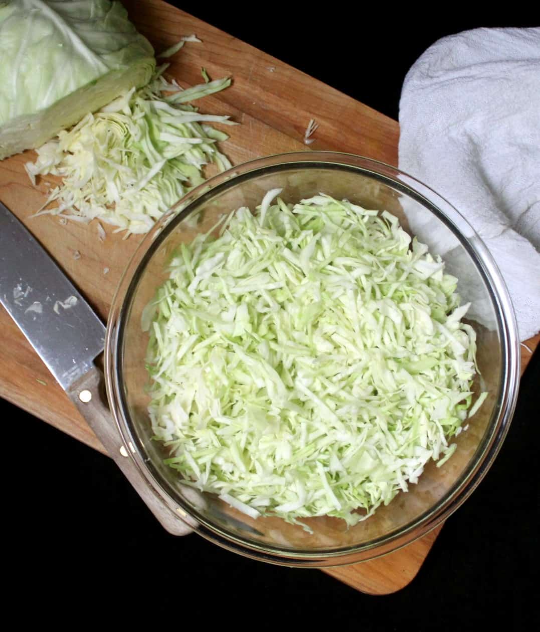 Finely shredded cabbage for sauerkraut in a bowl with a knife and chopping board