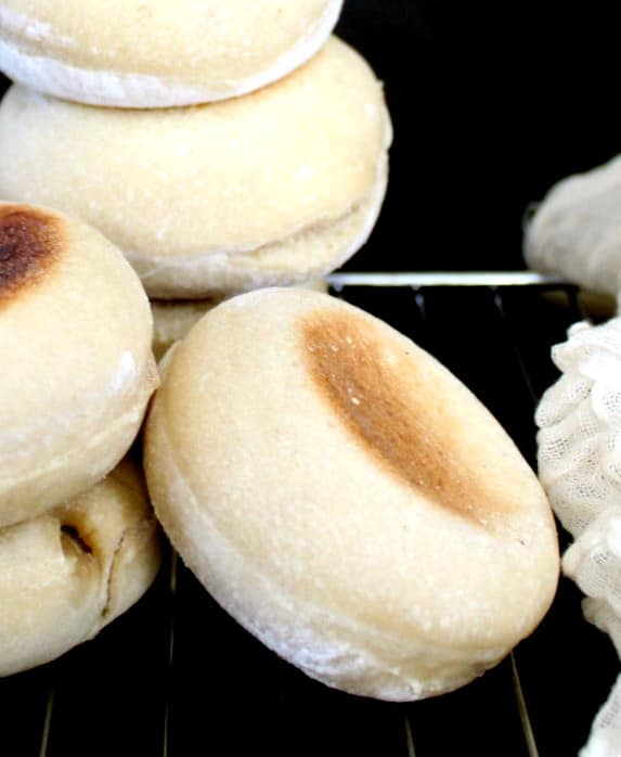 Close up of a single sourdough english muffin on a rack against a black background